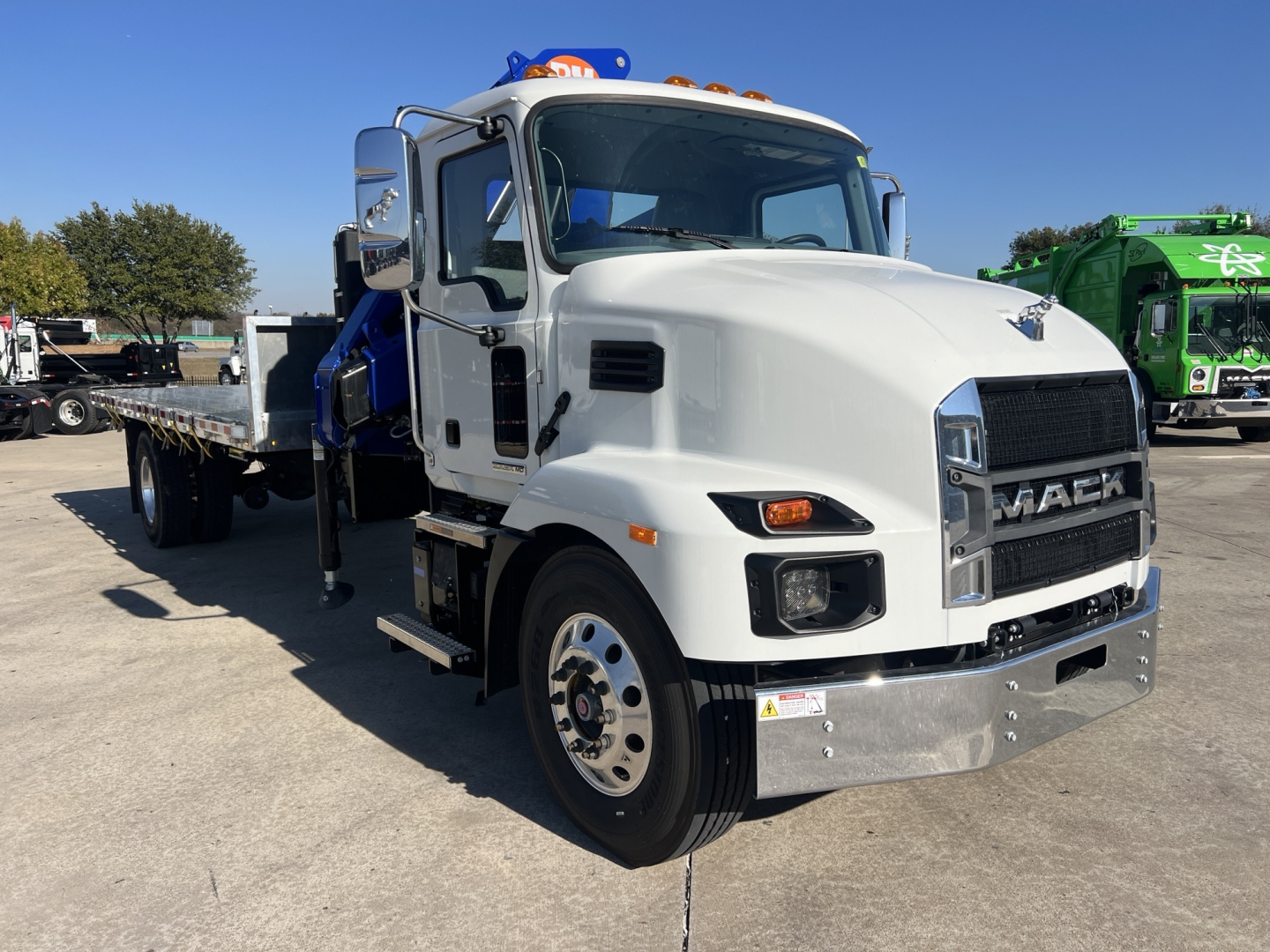Mack MD7 truck with white cab and chassis showing chrome grille and front bumper, flatbed behind cab, in a dealership lot.
