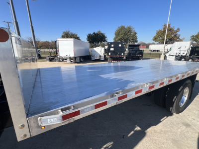 Flatbed New 2025 Mack MD7 truck bed with aluminum deck and reflective red/white safety tape along edges, dual rear wheels visible.