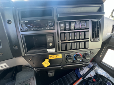 Mack MD7 cab interior showing dash with radio, multiple switches, and control knobs; labeled yellow tag near lower center.