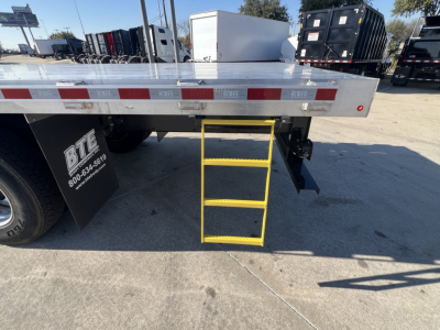 Flatbed truck rear with yellow step ladder, Mack MD7 information not visible; steel flatbed with reflective tape and bumper; stock number 67581 area not legible; blue sky.