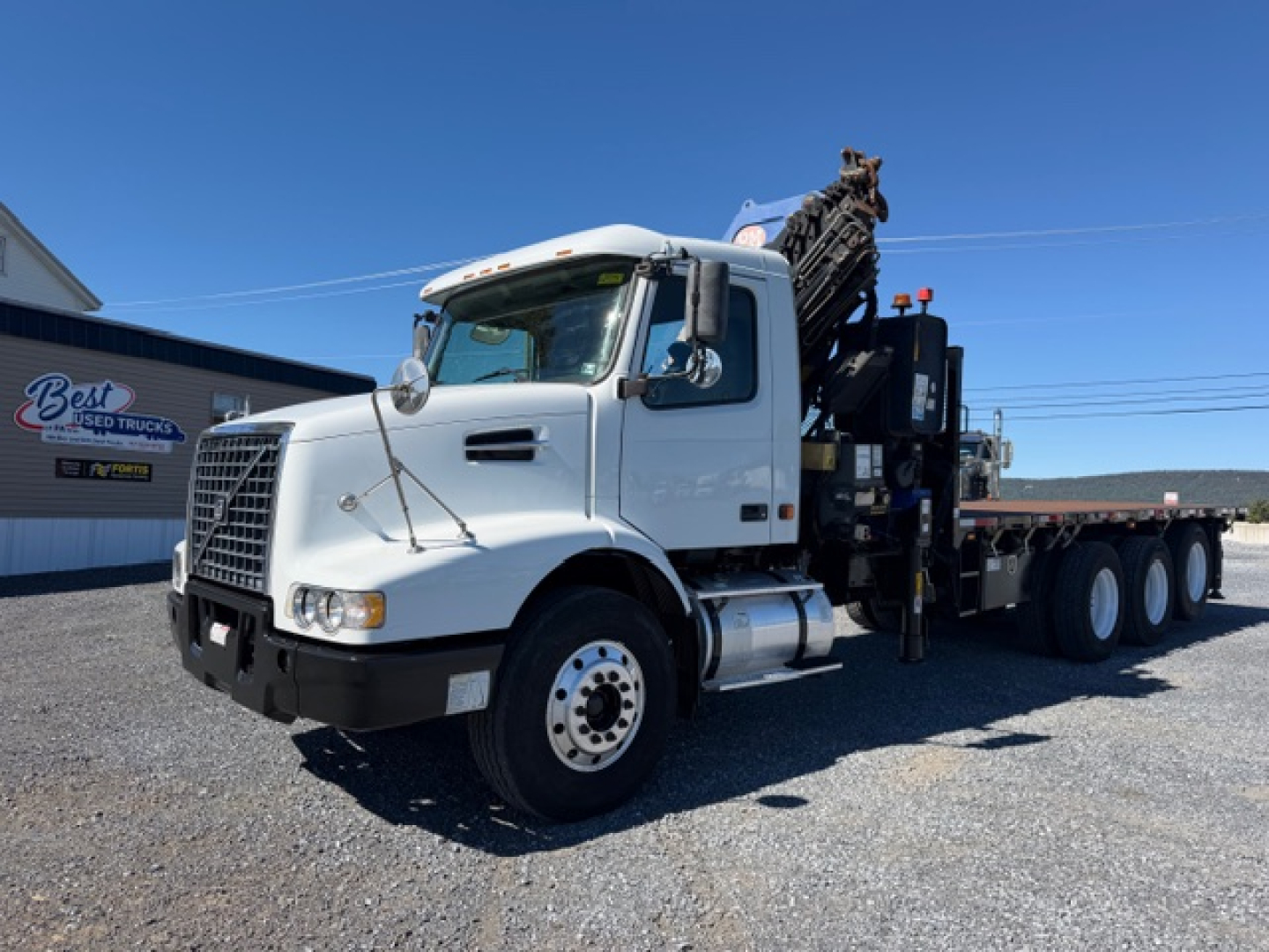 Volvo VHD crane truck in a parking lot with extended crane equipment on flatbed; front grille with Volvo emblem, side mirrors, and white cab.