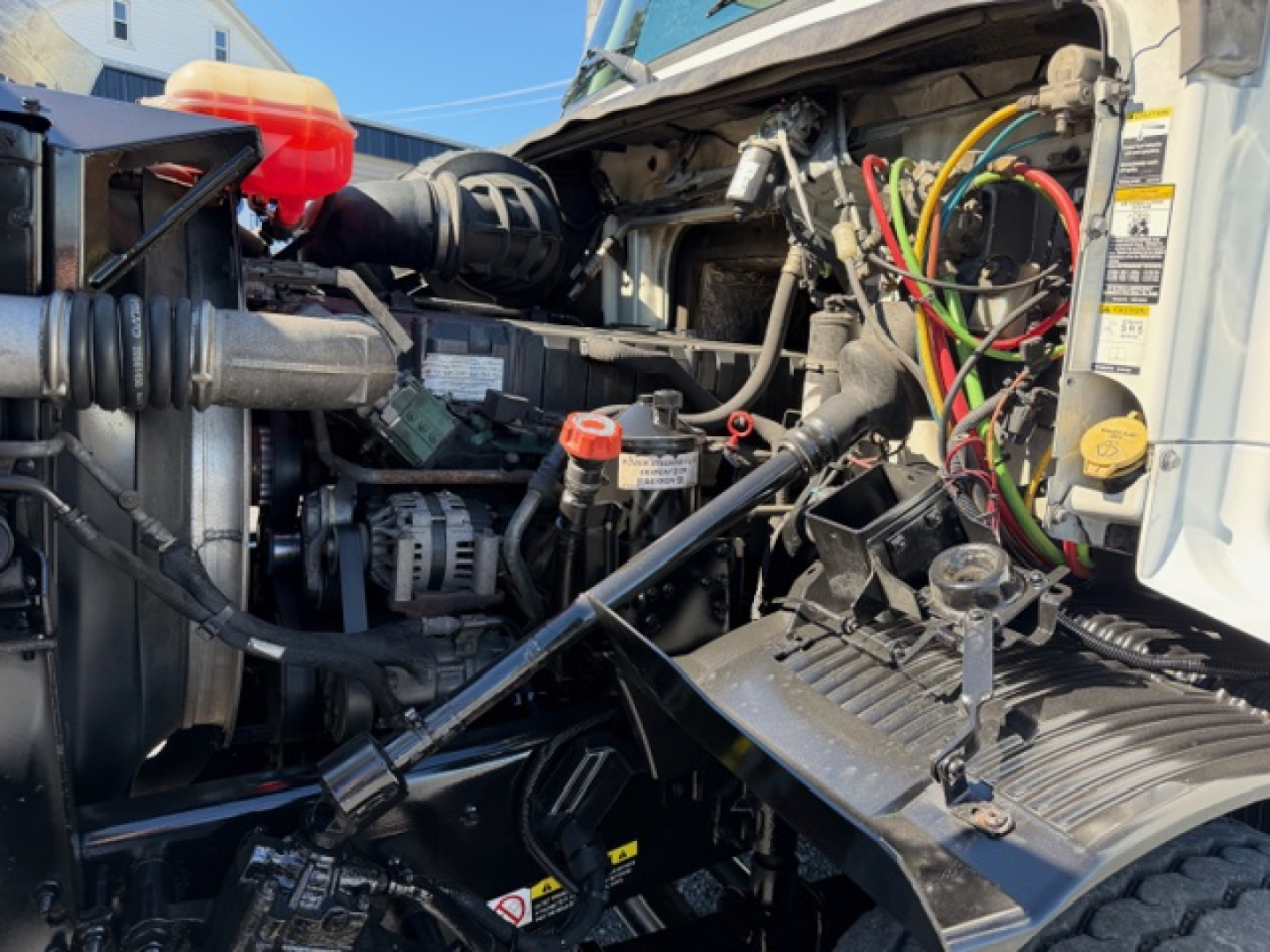 Volvo VHD crane truck engine bay showing multiple colored hoses, wiring harnesses, and labels on the firewall side.