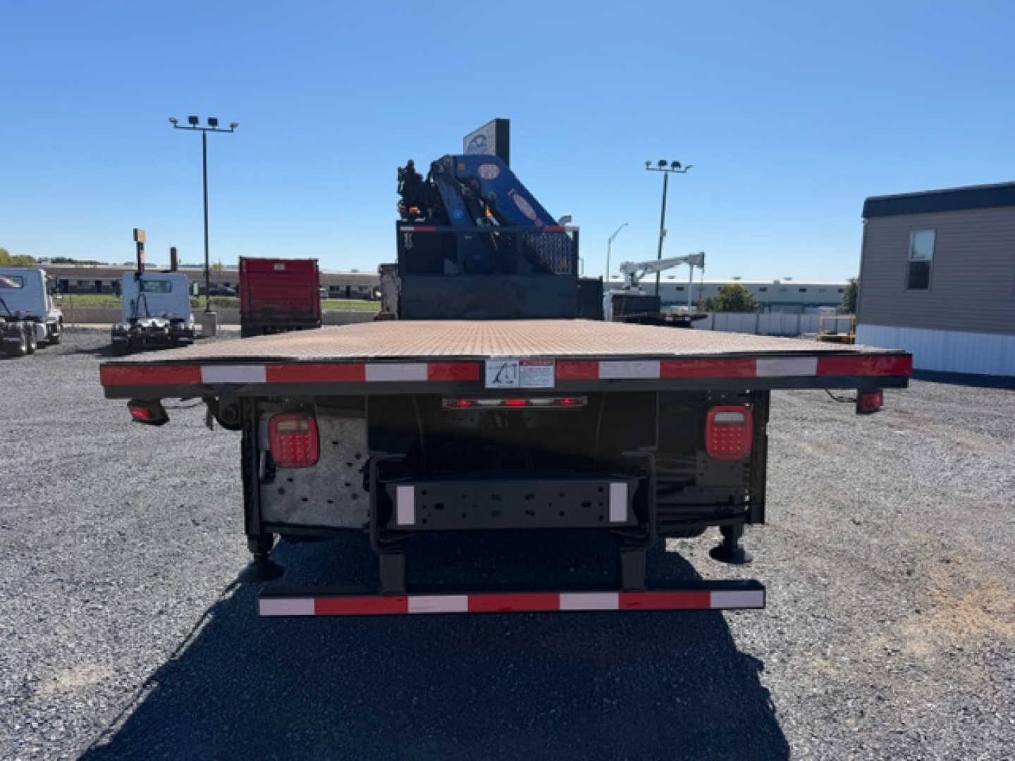 Flatbed tow truck with crane attachment at rear, rear view showing bumper, lights, and deck hardware.