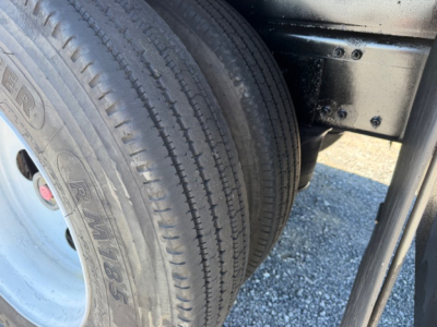 Truck wheel and underside showing dual rear tires with Rim decal, and part of chassis frame and suspension mounting.