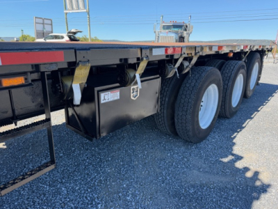 Volvo VHD crane truck side view showing underbody toolbox with sticker, triple axle rear, flatbed trailer and wheels.