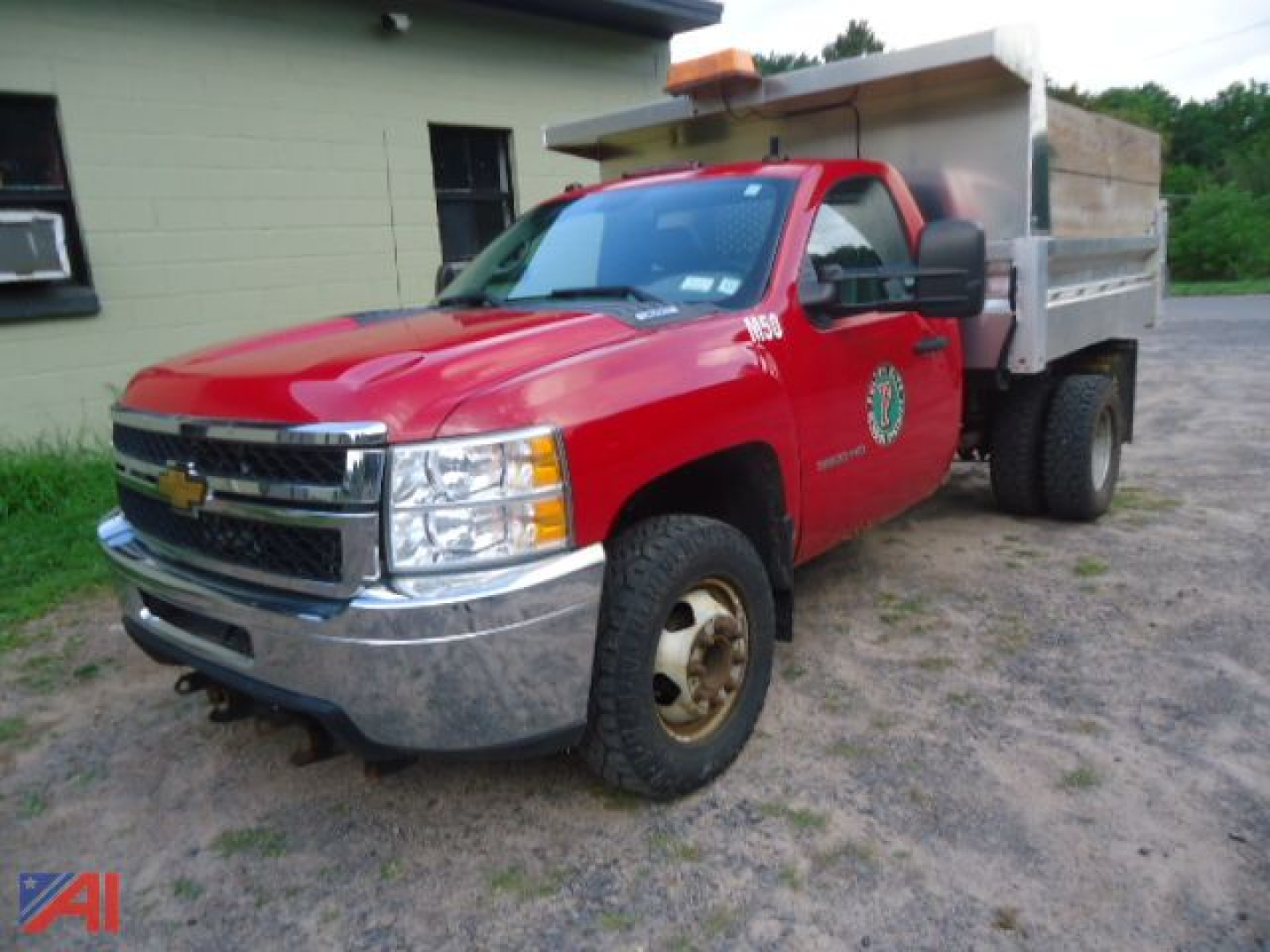 Chevrolet Silverado 3500HD dump truck with red cab and silver dump bed, front grille with gold bowtie emblem, side badge, large side mirrors, orange beacon on cab roof.