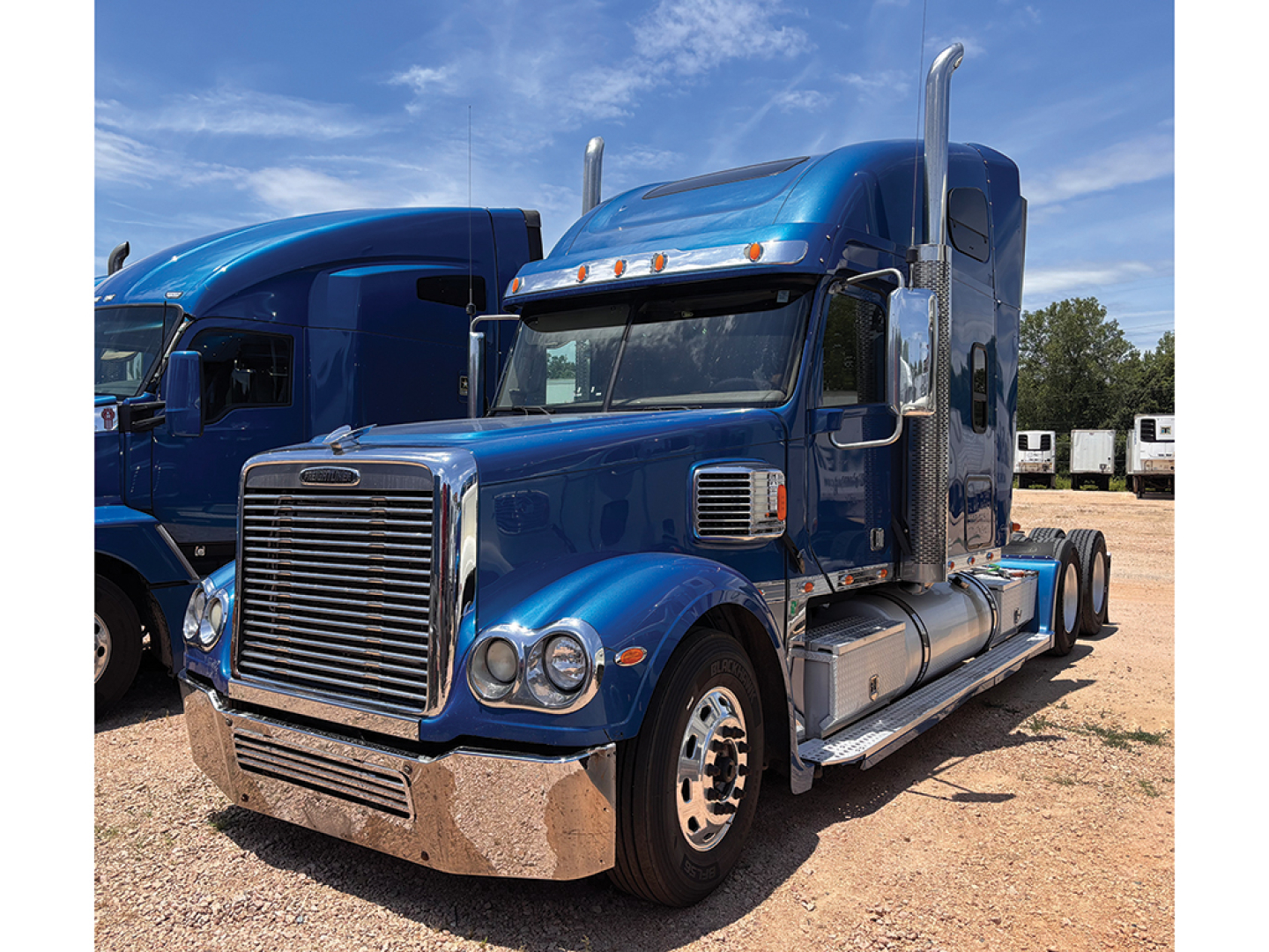 Freightliner Coronado semi-truck tractor in blue viewed from front-right profile showing chrome grille, headlights, and side steps.