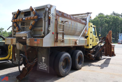 Freightliner 114 SD dump truck chassis with plow in yard, rear dump body and hydraulic system visible.
