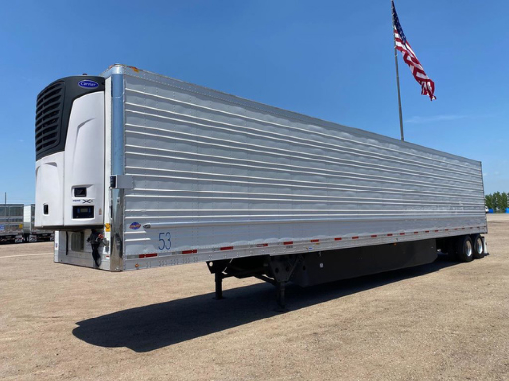 Trailer side view showing a refrigerated trailer with a mounted cooling unit at the front, metallic ribbed exterior, and landing gear visible.