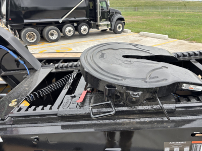 Jeep dolly trailer deck with circular spare wheel carrier and hydraulic components; black steel frame and coiled hoses; tag/labels visible on edge.