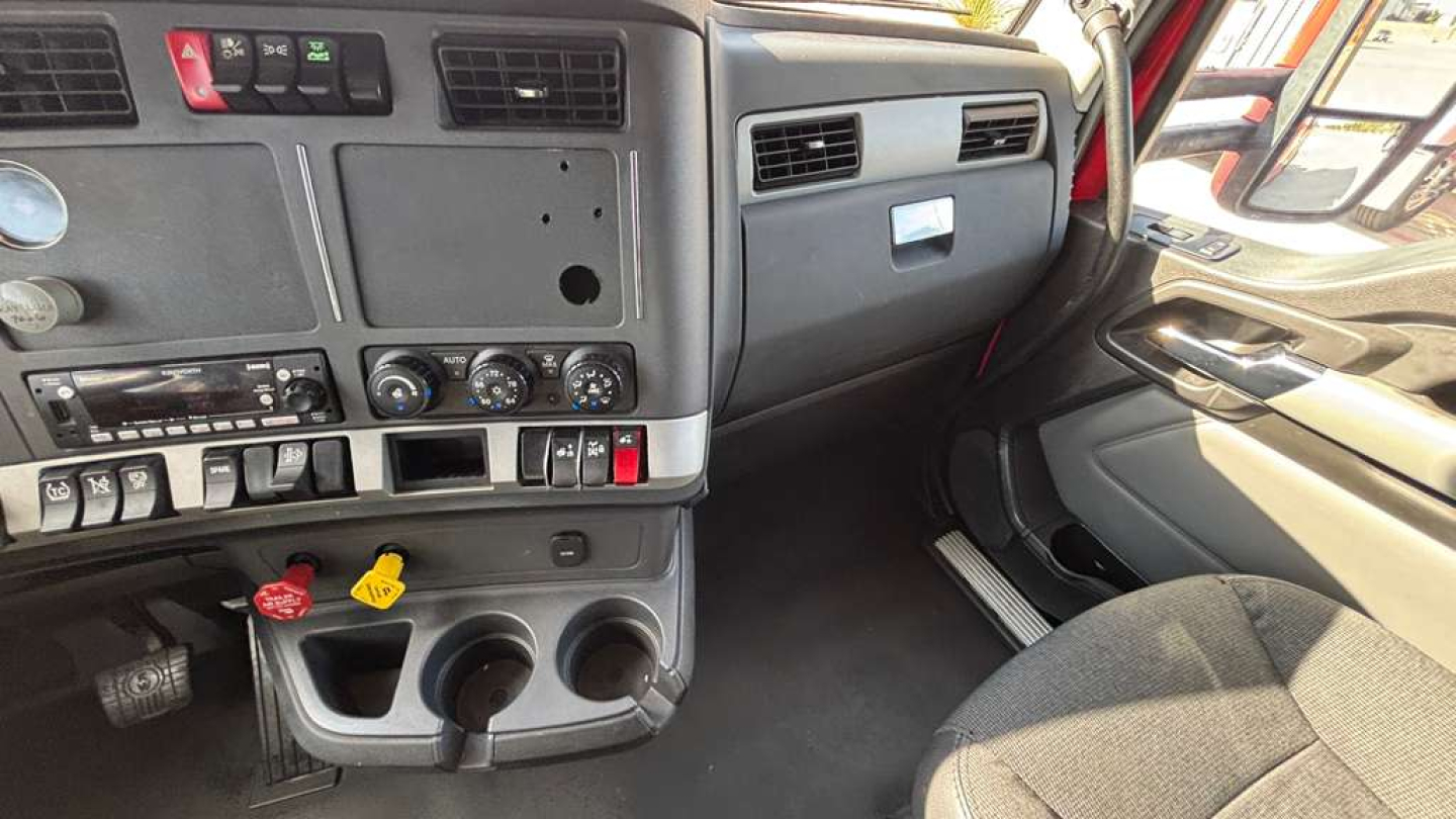 Kenworth T680 cab interior dash area showing center console, gauges, climate controls, steering wheel, and passenger-side door; driver seat visible.