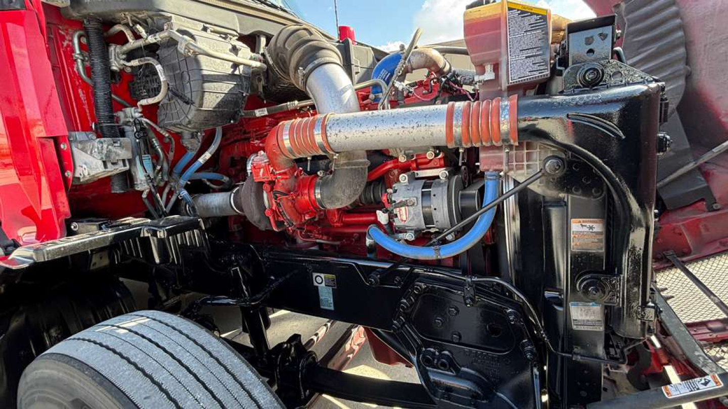 Kenworth T680 engine bay showing fuel lines, hoses, and radiator area with blue braided hose and red engine components.