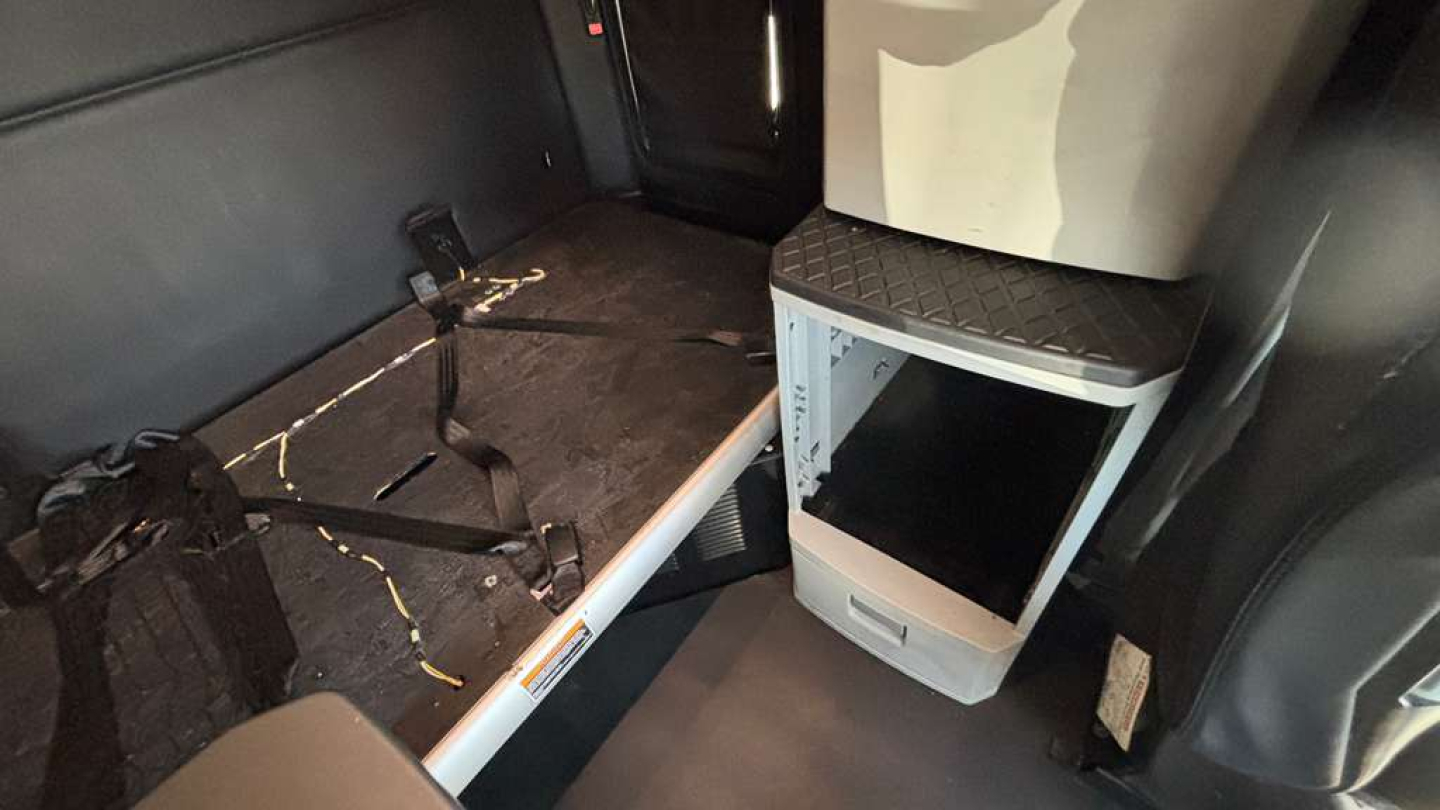 Kenworth T680 interior sleeper area with side cabinet and floor storage; view of cabin flooring and a small white cabinet with black screen.