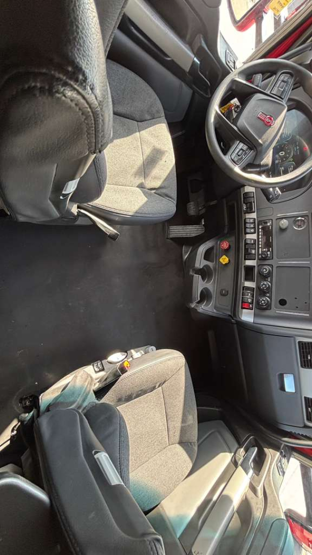Kenworth truck interior with steering wheel, dashboard, and seats visible; control panels and switches near center console.