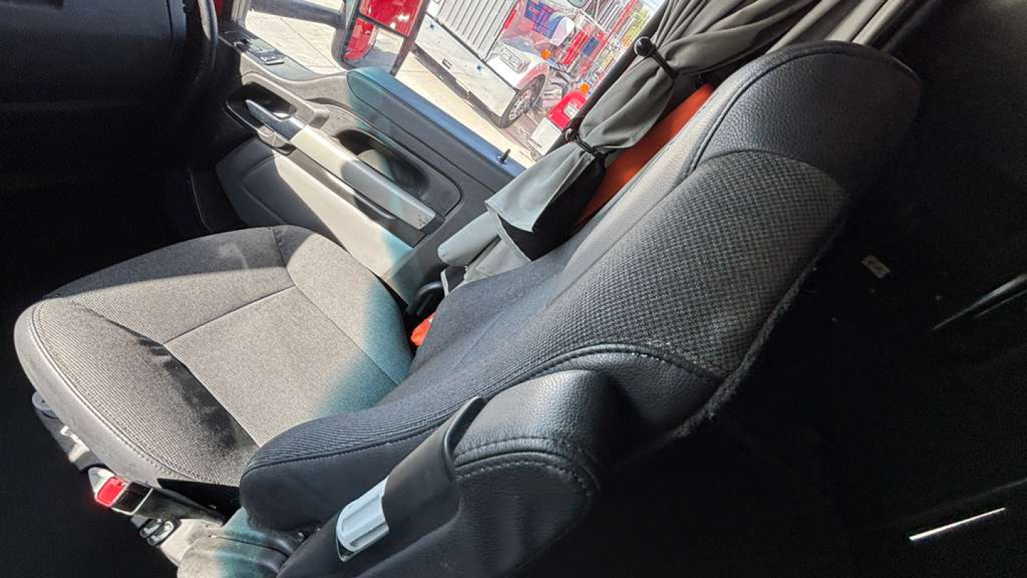 Kenworth T680 truck interior seat and door panel, driver seat with seat belt, grey fabric upholstery, window and control panel visible.