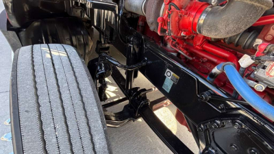 Kenworth T680 truck undercarriage showing chassis frame and dual rearides, with blue and red hoses and components near engine area.