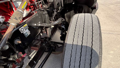 View of a Kenworth T680 engine bay area with suspension components and a large front tire visible.