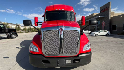 Truck front view showing large chrome grille with Kenworth emblem, red cab, black bumper, and side mirrors.