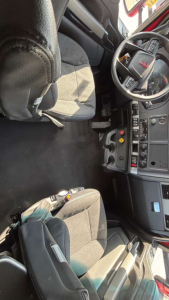 Kenworth truck interior with steering wheel, dashboard, and seats visible; control panels and switches near center console.