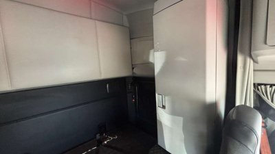 Interior of Kenworth truck cab with sleeper area and storage cabinet, dark panels, and a passenger seat visible.
