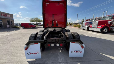 Kenworth T680 rear view showing fifth wheel, dual rear axles, mud flaps with MHC logo, and red sleeper cab in background.