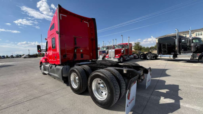 Kenworth T680 tractor truck chassis and cab in a truck lot, red cab, dual rear axles, standard fifth wheel area visible, used 2022 model.