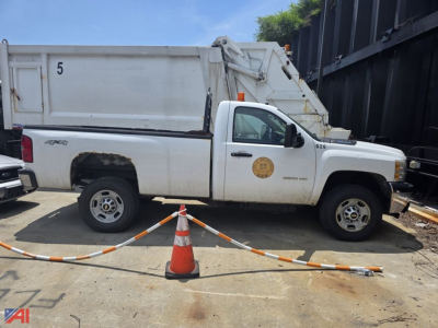 Side view of a white Chevrolet Silverado 2500HD utility/maintenance truck with a dump bed, 4x4, door emblem visible, parked on a lot with safety cones.