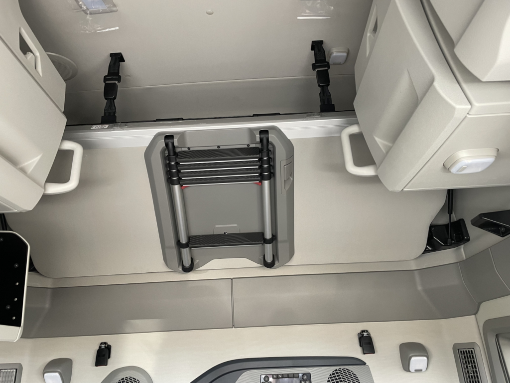 Truck interior showing a foldable step/ladder mounted on the cab floor with storage compartments and seating in view.