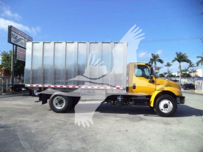 Truck in service bay with a yellow cab and silver dump bed side view showing cargo area and wheel wells.