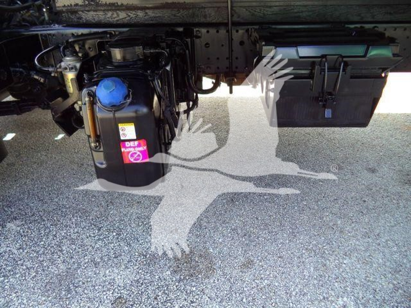 Isuzu NPRR undercarriage showing DEF/blue cap reservoir and battery box with wiring; side view of truck frame and toolbox.