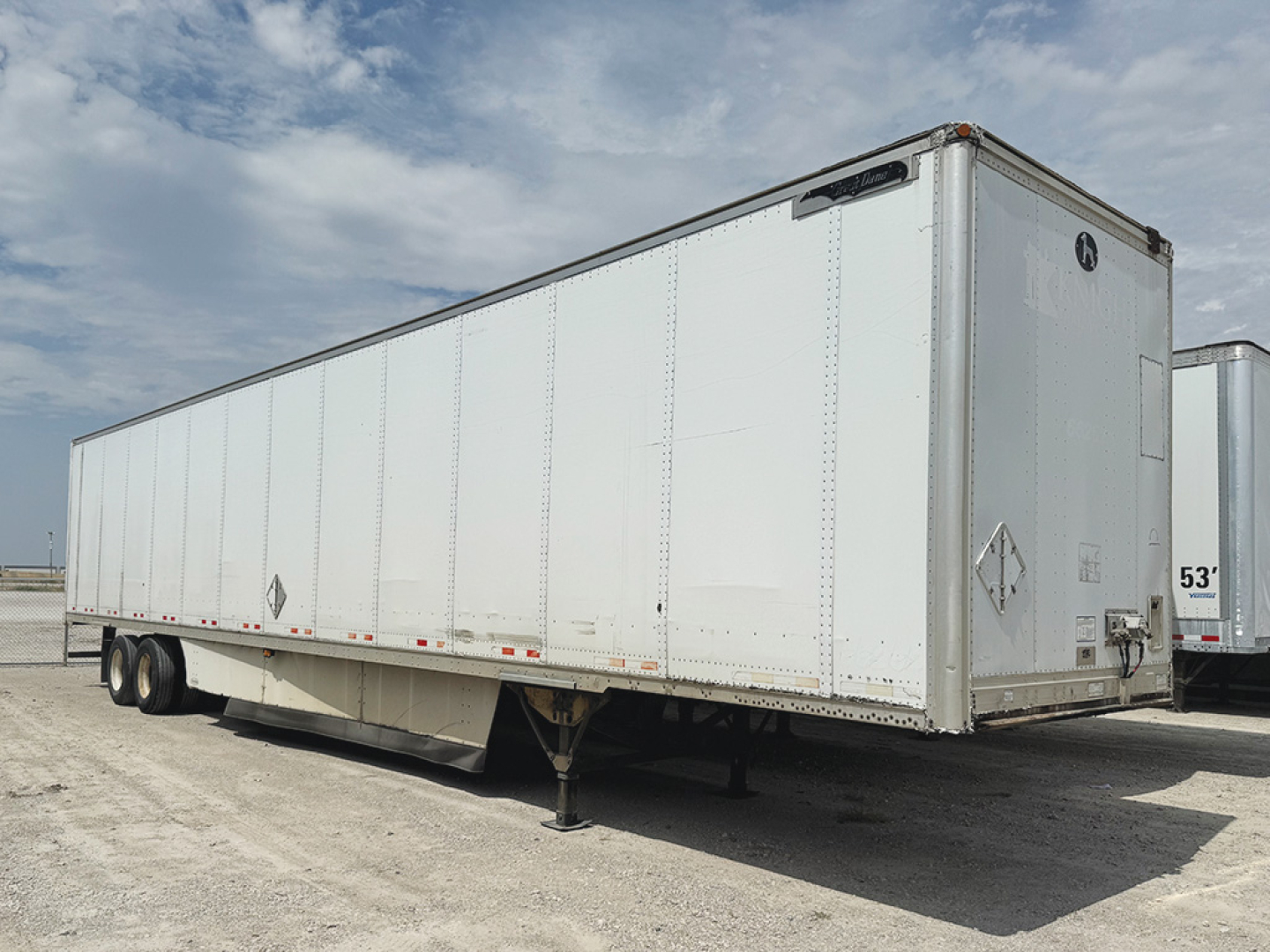 Long white Great Dane plate trailer, side view, undercarriage with drop legs, dual rear axles, diamond placards on front corner.