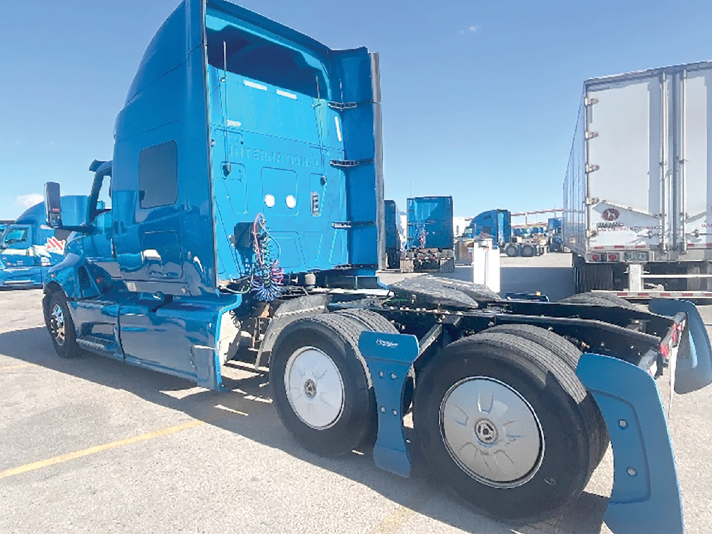 Truck cab and rear wheels of a blue 2020 International LT625 semi-truck in a parking lot, showing the sleeper cab and sixth wheel area.