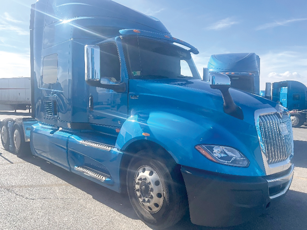 Blue 2020 International LT625 sleeper cab truck, elevated front grille with chrome accents, large side mirrors, dual rear axles, daytime running lights, parked in lot.