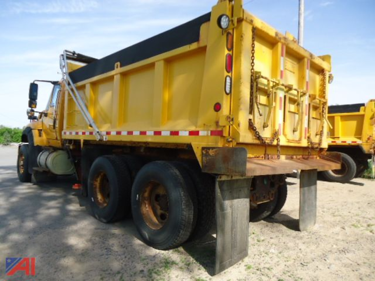Dump truck rear and side showing side spreader dump body with yellow paint, dual rear wheels, and mud flaps.