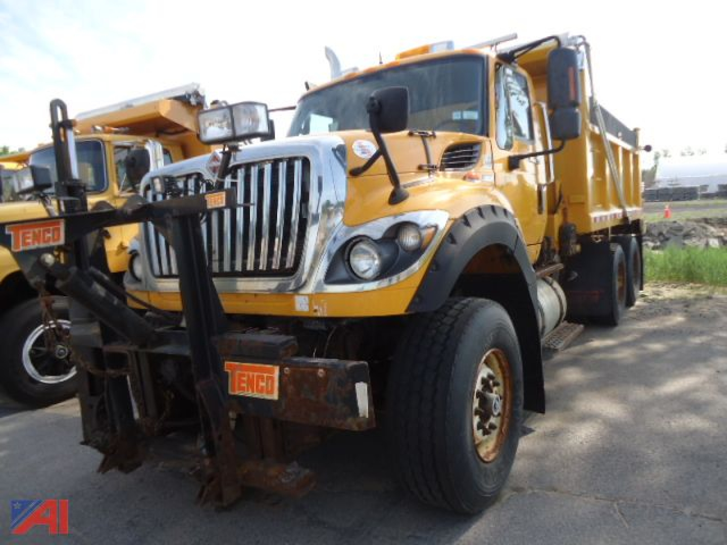 Dump truck with a front-mounted snow plow attachment or wing; yellow International WorkStar 7600 side spreader/dump truck in view showing front grille, large headlights, and heavy-duty tires.