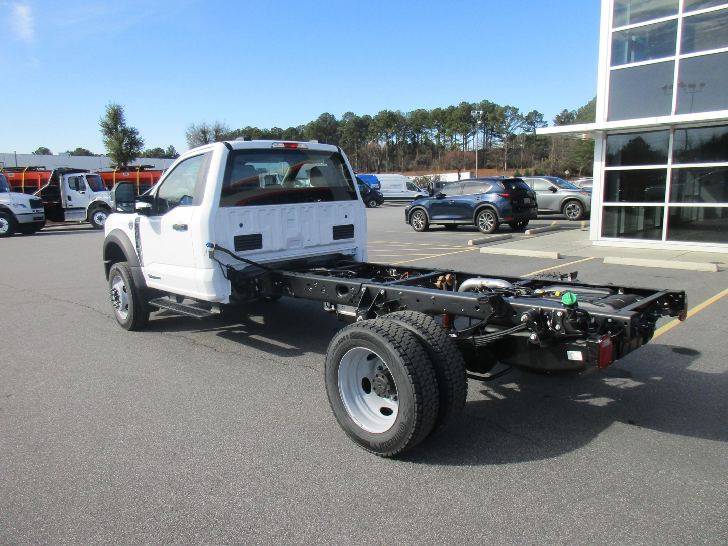 Ford F-450 cab and chassis with open rear frame showing chassis, single rear wheel, white cab, dealership lot in background.