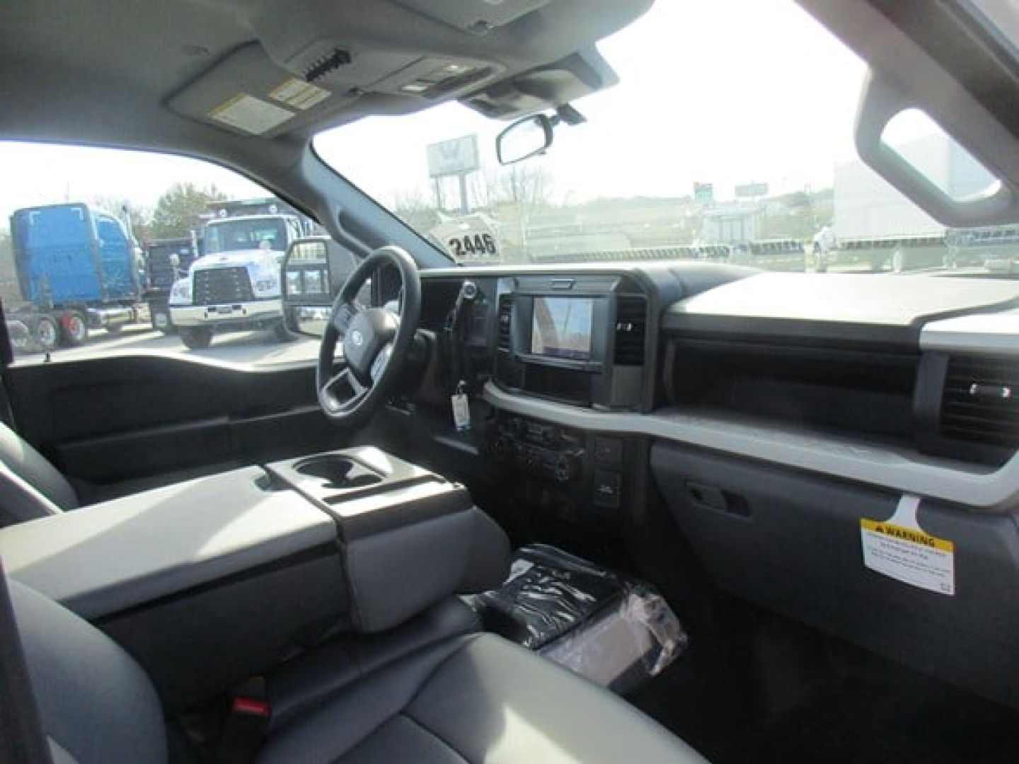 Cab and chassis truck interior view featuring steering wheel, center console touchscreen, and dashboard with storage bin; light gray upholstery and plastic trim.