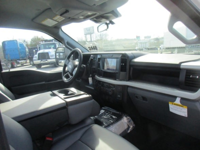 Cab and chassis truck interior view featuring steering wheel, center console touchscreen, and dashboard with storage bin; light gray upholstery and plastic trim.