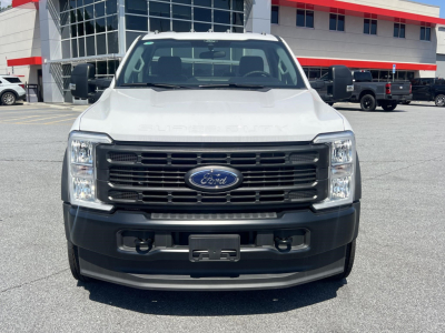 Front view of a white 2026 Ford F-450 cab and chassis truck in a dealership lot with black grille, Ford emblem, and bumper Visibility.