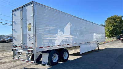 Reefer trailer in a lot showing a large side with a white eagle logo and tandem axle trailer gear; rear doors with metal bars and warning decals; no visible VIN text.