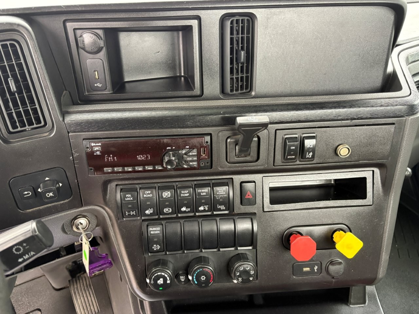 Dashboard of a 2019 International LT daycab showing controls, switches, and diagnostic panels. Visible components include ignition with key, air conditioning knobs, hazard switch, red and yellow trailer connections, and a radio/climate pane