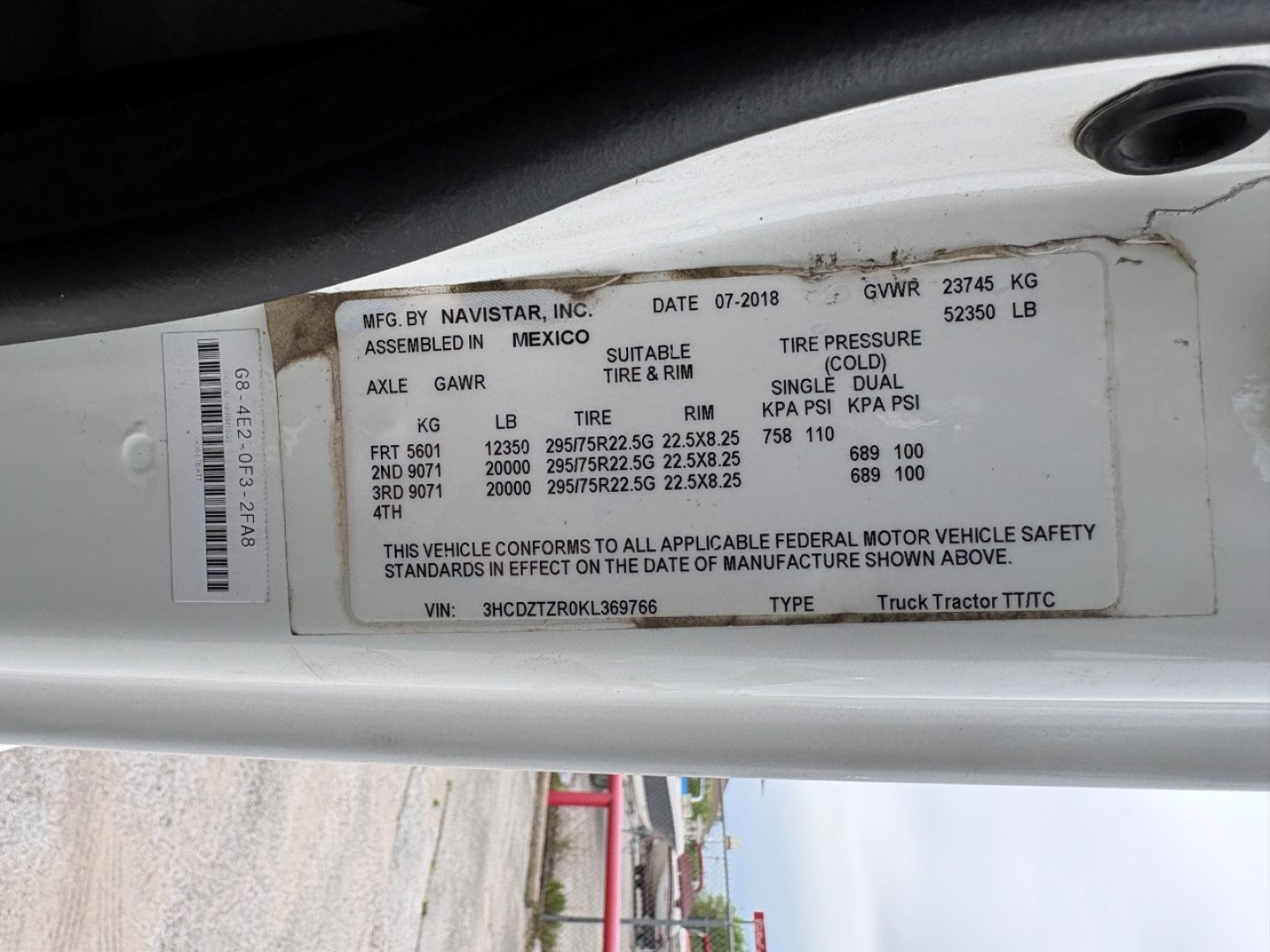 Label on door jamb with VIN, stock number, and GVWR details for a 2019 International LT Daycab truck. Text includes MFG BY NAVISTAR INC, MEXICO assembly, axle GAWR, tire sizes, TIRE PRESSURE, and vehicle safety standards. VIN 3HCDZTZR0KL369