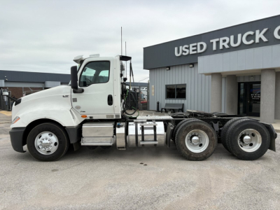Truck side view of a white 2019 International LT conventional daycab, showing cab and chassis with fuel tanks and dual rear axles, at a used truck lot.