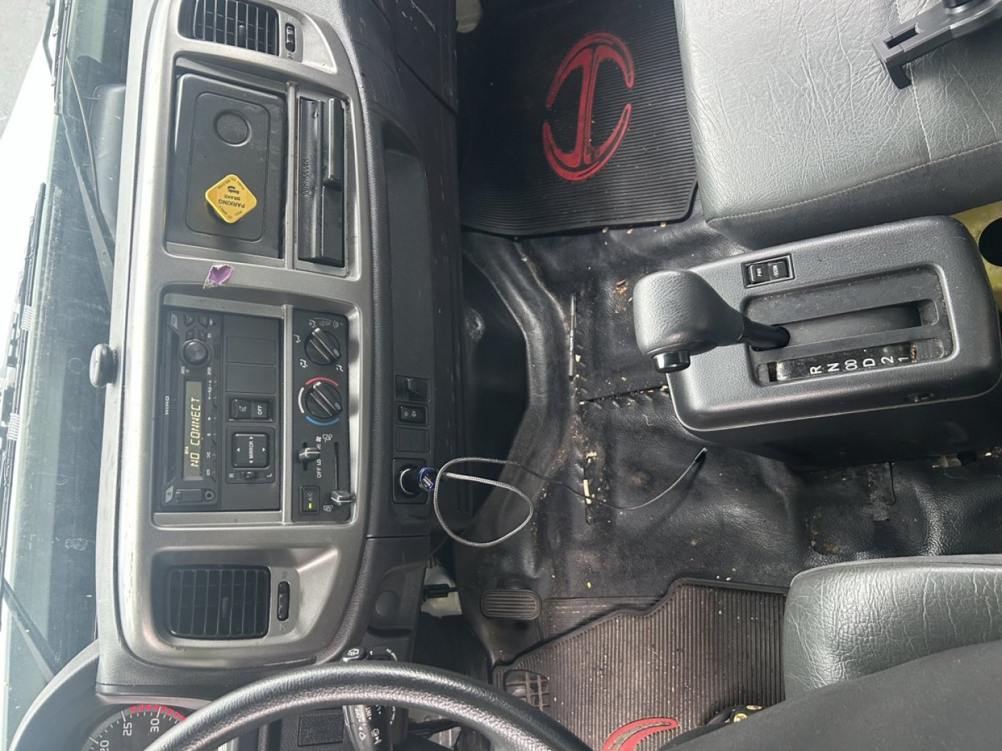 Inside cab of a 2019 Hino 268 showing dashboard controls, steering wheel, gear shifter, and floor with scattered debris.
