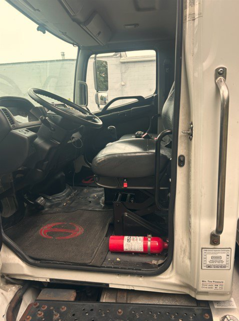 Cab interior of a 2019 Hino 268 box van truck showing driver's seat, steering wheel, pedals, and a fire extinguisher on the floor mat.