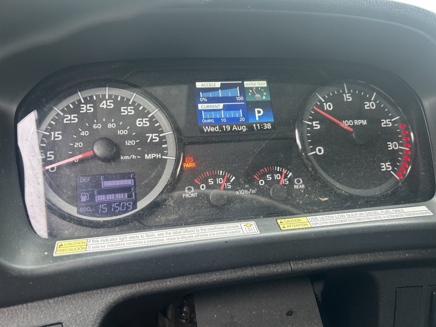 Dashboard of a 2019 Hino 268 showing gauges: speedometer 0-105 mph with km/h inner, tachometer up to 35? RPM, digital display with time and date, warning icons, fuel/temp gauges.
