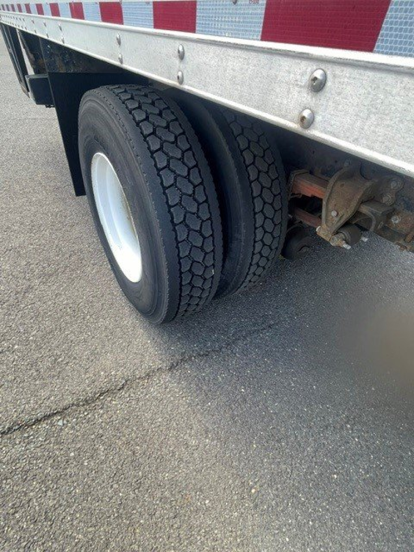 Rear wheel assembly of a box van truck showing dual tires and metal underride guard with reflective side rails.