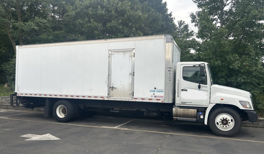 Truck side view of a 2019 Hino 268 box van with a large rectangular cargo box. Visible text includes GVW or logos on the cab door and a small logo near the rear wheel.