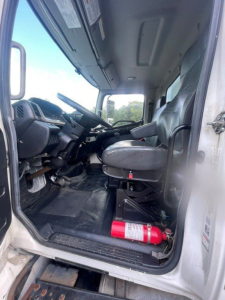Box van truck cab interior with steering wheel, driver seat, dashboard, and a fire extinguisher on the floor.