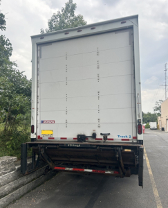 Back of a white Hino box truck with a liftgate, showing Morgan lift label and rear lights. Small Morgan sticker and truck 2 label at bottom of cargo door.